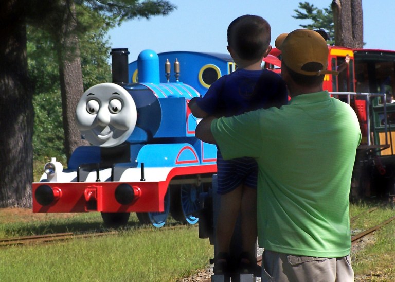 In this 2012 photo provided by Edaville USA, a father and son watch Thomas the Tank Engine roll down the track at an annual Day Out with Thomas event at the Edaville USA theme park in Carver, Mass. Groundbreaking for the first permanent Thomas Land in the the United States is set for July 2014 at Edaville USA, and is expected to be open for business in the summer of 2015. (AP Photo/Edaville USA)