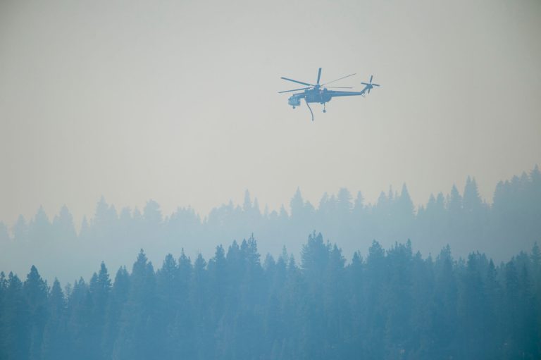 In this Wednesday, Sept. 24, 2014 photo, smoke from the King Fire fills the air as a helicopter prepares to refill with water near the Union Valley Reservoir in El Dorado County, Calif. Heavy rains this week and the prospect of more wet weather over the weekend are raising hopes that firefighters will get full containment quickly on the massive wildfire in a heavily forested region of the Sierra east of Sacramento. (AP Photo/The Sacramento Bee, Randall Benton)