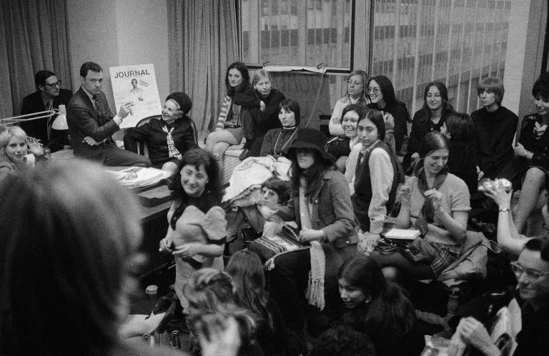 FILE- In this March 18, 1970 file photo, Ladies' Home Journal editor John Mack Carter sits on his desk while surrounded by a group of feminists in his New York office who were seeking his resignation so that he could be replaced by a woman. Carter, who led some of the nation's most popular women's magazines through the height of the women's rights movement, died at his home in Bronxville, N.Y., Friday, Sept. 26, 2014, at age 86, Hearst Corp. announced. (AP Photo/SJ, File)