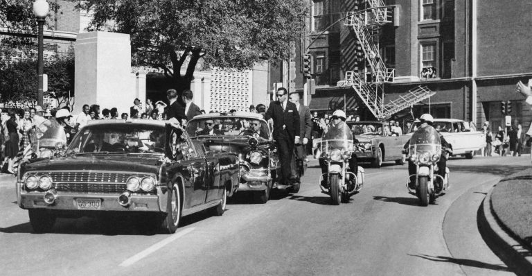 President John F. Kennedy's hand reaches toward his head within seconds of being fatally shot as first lady Jacqueline Kennedy holds his forearm as the motorcade proceeds along Elm Street past the Texas School Book Depository in Dallas on Nov. 22, 1963. (AP Photo/James W. 