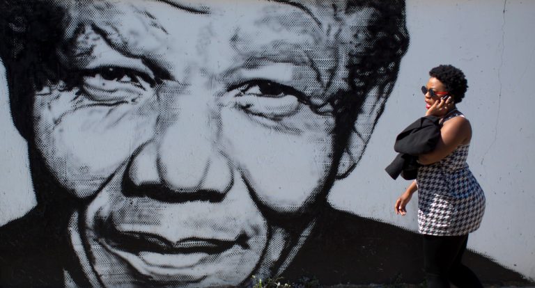 A South African woman talks on her mobile phone as she walks past a mural depicting the late former South African President Nelson Mandela, in the Soweto township on the outskirts of Johannesburg, South Africa Friday, May 2, 2014. South African political parties hold final campaign rallies this weekend ahead of elections on Wednesday, May 7, 2014 that are likely to see the ruling African National Congress return to power with a smaller majority due to voters disaffected by corruption in government and economic inequality. (AP Photo/Ben Curtis)