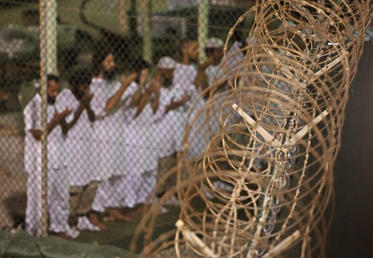 Guantanamo detainees pray before dawn near a fence of razor-wire, inside Camp 4 detention facility at Guantanamo Bay U.S. Naval Base, Cuba, on May 14, 2009. A formal review process for dozens of men being held at Guantanamo Bay without charge has begun as part of an effort to close the prison, the Pentagon said Wednesday. (AP Photo/Brennan Linsley, File)