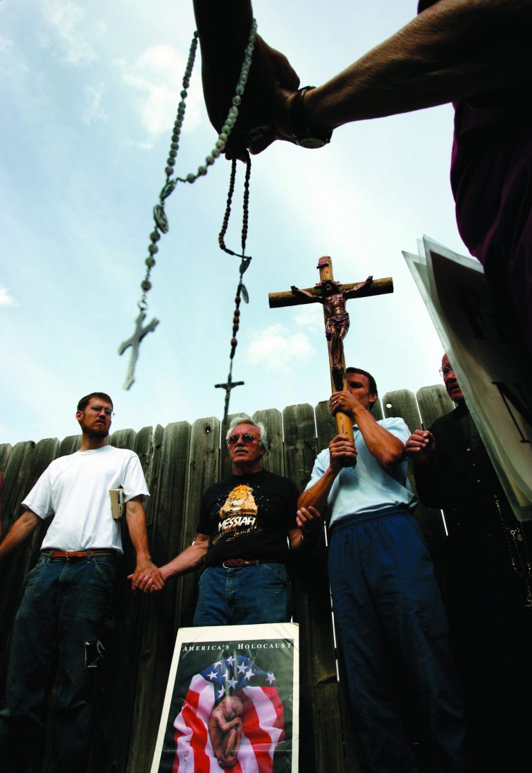 FILE - In this Thursday, May 17, 2007 file photo, Richard Mahoney, right, Eugene Frye, center, and Michael, left, and others pray on the first day of Operation Rescue's 77-hour prayer vigil at Women's Health Care Services, a clinic operated by Dr. George Tiller, in Wichita, Kan. Tiller was one of the few remaining late-term abortion providers in the nation when he was murdered. (AP Photo/Larry W. Smith, File)
