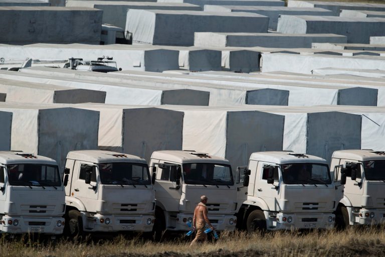A driver carries empty water bottles as he walks past trucks forming part of an aid convoy parked in a field about 28 kilometers (17 miles) from the Ukrainian border, near Kamensk-Shakhtinsky, Rostov-on-Don region, Russia, Saturday, Aug. 16, 2014. Hundreds of trucks in a Russian aid convoy are waiting near the Ukrainian border as complicated procedures drag on for allowing them into eastern Ukraine to help civilians suffering amid fighting between Ukrainian forces and separatists. (AP Photo/Pavel Golovkin)