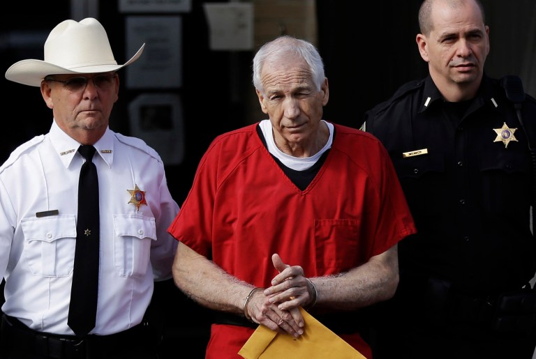   FILE - In this Oct. 9, 2012 file photo, former Penn State University assistant football coach Jerry Sandusky, center, is taken from the Centre County Courthouse by Centre County Sheriff Denny Nau, left, and a deputy, after being sentenced in Bellefonte, Pa. Sandusky was sentenced to at least 30 years in prison, effectively a life sentence, in the child sexual abuse scandal that brought shame to Penn State and led to coach Joe Paterno's downfall. The Sandusky saga was a top story in the sports world in 2012. (AP Photo/Matt Rourke, File)  