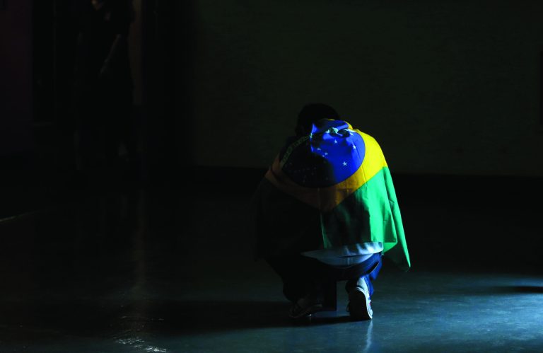 A volleyball fan wearing Brazil's flag kneels by a doorway before the start of a women's gold medal volleyball match between the United States and Brazil at the 2012 Summer Olympics, Saturday, Aug. 11, 2012, in London. (AP Photo/Jeff Roberson)