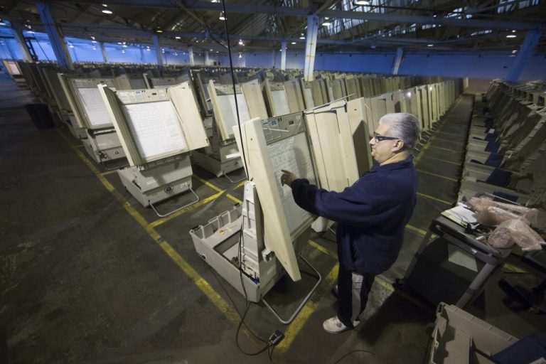 Endless rows of digital voting machines are seen with one man selecting his vote on a close machine.
