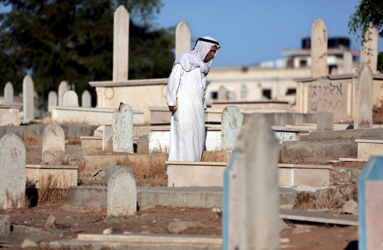 An elderly Palestinian man stands above a grave of one of his relatives in a cemetery next to Hebrew graffiti during the Eid al-Adha holiday in Gaza City, Saturday, Oct. 4, 2014. Muslims around the world Saturday celebrated Eid al-Adha to commemorate the willingness of the prophet Ibrahim - or Abraham as he is known in the Bible - to sacrifice his son in accordance with God's will, though in the end God provides him a sheep to sacrifice instead. The major Muslim holiday coincides this year with the Jewish holiday of Yom Kippur, the first time this has happened since 1981. (AP Photo/Khalil Hamra)