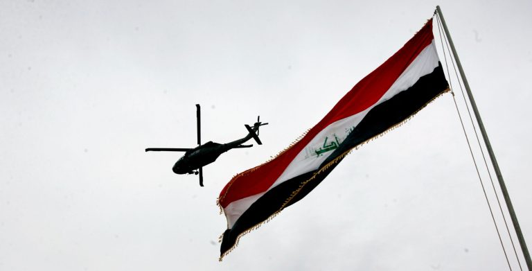 A U.S. Army helicopter flies over an Iraqi flag during a handover ceremony at Camp Rustimiyah March 31, 2009 in Baghdad. (Photo by Wathiq Khuzaie/Getty images)