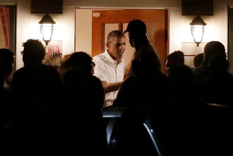 President Barack Obama, center, speaks with people on the porch while visiting with Valerie Jarrett and friends in Oak Bluffs, Mass., on the island of Martha's Vineyard, Friday, Aug. 22, 2014. Obama is vacationing for about two weeks on the island. (AP Photo/Steven Senne)