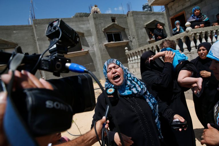 A Palestinian mourner cries as she talks to a TV  journalist, while the bodies of Mousa Abu Muamer, 56, and his son Saddam, 27, who were killed in an overnight Israeli missile strike at their house are brought in during their funeral procession, on the outskirts of the town of Khan Younis, southern Gaza Strip, Monday, July 14, 2014. Saddam's wife Hanadi, 27, was also killed in the attack. (AP Photo/Lefteris Pitarakis)