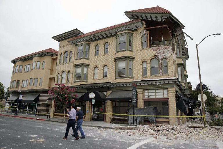 Two men walk past the earthquake-damaged building that housed the Carpe Diem wine bar  Monday, Aug. 25, 2014, in Napa, Calif. The San Francisco Bay Area's strongest earthquake in 25 years struck the heart of California's wine country early Sunday, igniting gas-fed fires, damaging some of the region's famed wineries and historic buildings, and sending dozens of people to hospitals. (AP Photo/Eric Risberg)