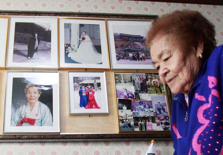 In this Feb. 3. 2014, Kim Gun-ja, 89, former comfort woman who was forced to serve for the Japanese troops as a sex slave during World War II, passes by her wedding picture, top center, at the House of Sharing, a nursing home and museum for 10 former sex slaves, in Toechon, South Korea. There are only 55 women left who registered with the South Korean government as former sex slaves from the war _ down from a peak of more than 230. Their average age is 88. (AP Photo/Ahn Young-joon)