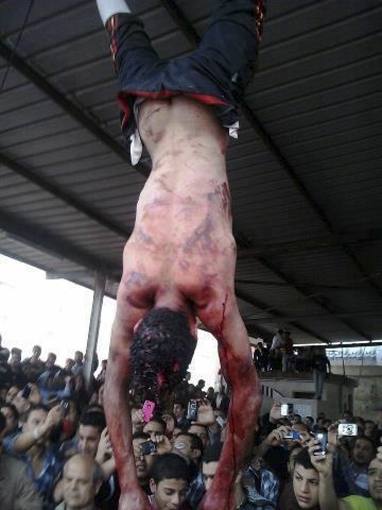 EDS NOTE GRAPHIC CONTENT -- Egyptians surround the bodies of two men hung by their feet in a bus station after being accused of theft in Samanod, about 55 miles (90 kilometers) north of Cairo, Egypt, Sunday March 17, 2013. Egyptian vigilantes beat two men accused of stealing a motorized rickshaw, stripped them half-naked and hung them by their feet in a crowded bus station in the Nile Delta on Sunday, according to security officials. Both men died.The killings came a week after the attorney general's office encouraged civilians to arrest lawbreakers and hand them over to police. (AP Photo)