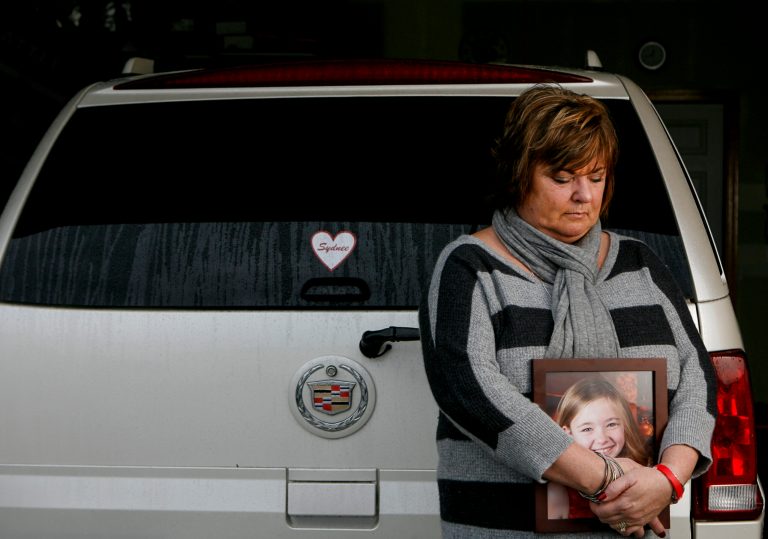   In this Saturday, Dec. 22, 2012 photo, Judy Neiman holds a photo of her daugher, Sydnee, in front of her 2006 Cadillac Escalade at her home in West Richland, Wash. Sydnee died in late 2011 after Neiman accidentally backed over her with the SUV. Although there is a law in place that calls for new manufacturing requirements to improve the visibility behind passenger vehicles, the standards have yet to be mandated because of delays by the U.S. Department of Transportation. (AP Photo/Kai-Huei Yau)  
