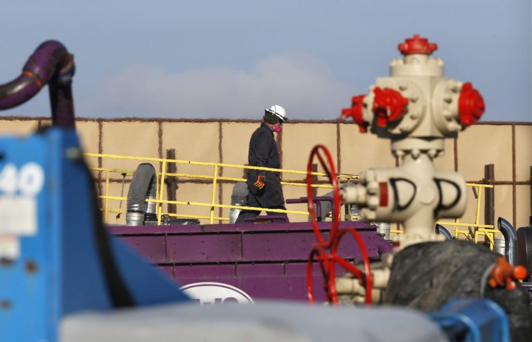 In this March 25, 2014 photo, a worker watches over a hydraulic fracturing operation at an Encana  Corp. gas well, near Mead, Colo. In the background is a tall canvas wall around the perimeter of the extraction site, which mitigates noise, light and dust coming from the operation during the drilling and completion phase, which generally takes a few weeks. (AP Photo/Brennan Linsley)