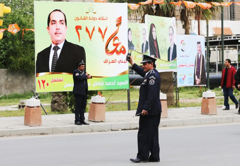Iraqi traffic police officers control traffic in front of election campaign posters in Baghdad, Iraq,Tuesday April 1, 2014. The election campaign kicked off Tuesday with Iraqi towns and cities flooded with posters of the candidates for parliament seats on main streets and intersections. (AP Photo/Karim Kadim)