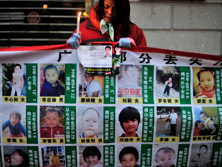 FILE - In this Jan. 24, 2010 file photo, a woman holds a candle behind a board showing photos of missing children during a campaign to spread the information to search for them in Wuhan, in central China's Hubei province. Chinese police have rescued 382 abducted babies and arrested 1,094 suspects in a national operation that busted four major Internet-based, baby-trafficking rings, the Public Security Ministry said Friday, Feb. 28, 2014. (AP Photo, File)  CHINA OUT