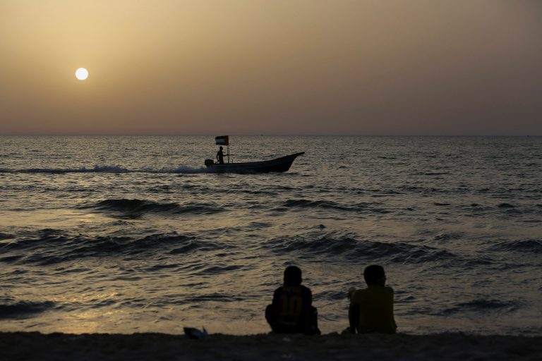 FILE - In this Friday, May 30, 2014 file photo, Palestinians enjoy the beach on the Mediterranean Sea as a fisherman sails on his boat at sunset in Gaza City, in the northern Gaza Strip. The Israeli navy arrested four Palestinian fishermen and seized their boat on Tuesday, Sept. 9, 2014, a Gaza official says, in one of the first instances of friction between the sides since the Gaza war ended last month. The Israeli military said two vessels were involved in the incident. It said the vessels were operating outside of their permitted maritime limit, and after ignoring requests to move closer to shore were boarded by naval personnel and seized. (AP Photo/Adel Hana, File)