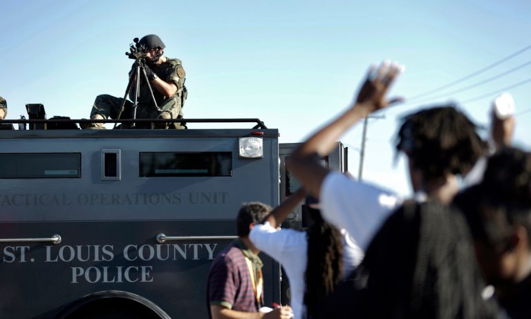 A member of the St. Louis County Police Department points his weapon in the direction of a group of protesters in Ferguson, Mo. on Wednesday, Aug. 13, 2014. On Saturday, Aug. 9, 2014, a white police officer fatally shot Michael Brown, an unarmed black teenager, in the St. Louis suburb. (AP Photo/Jeff Roberson)