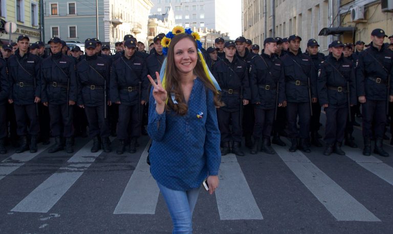 A woman wearing traditional Ukrainian flower headband poses for a photo in front of police officers, during an anti-war rally in downtown Moscow, Russia, Sunday, Sept. 21, 2014. Thousands of people were marching through central Moscow to demonstrate against the fighting in Ukraine. (AP Photo/Denis Tyrin)