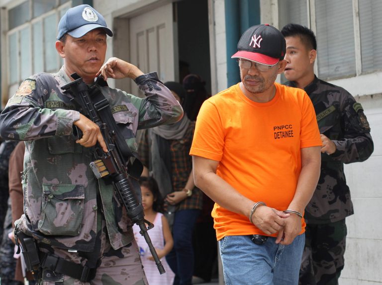 FILE - In this Friday, June 20, 2014 file photo, a Philippine police officer escorts Abu Sayyaf extremist group leader Khair Mundos, right, after his arraignment at courts inside a police camp in Taguig City, south of Manila, Philippines.  The captured Abu Sayyaf commander has told investigators that a top Southeast Asian terror suspect, who the military reported was killed in a U.S.-backed airstrike two years ago, is alive and being harbored by a hardline Muslim rebel group in the southern Philippines, a confidential police report said. (AP Photo/Mark Cristino)
