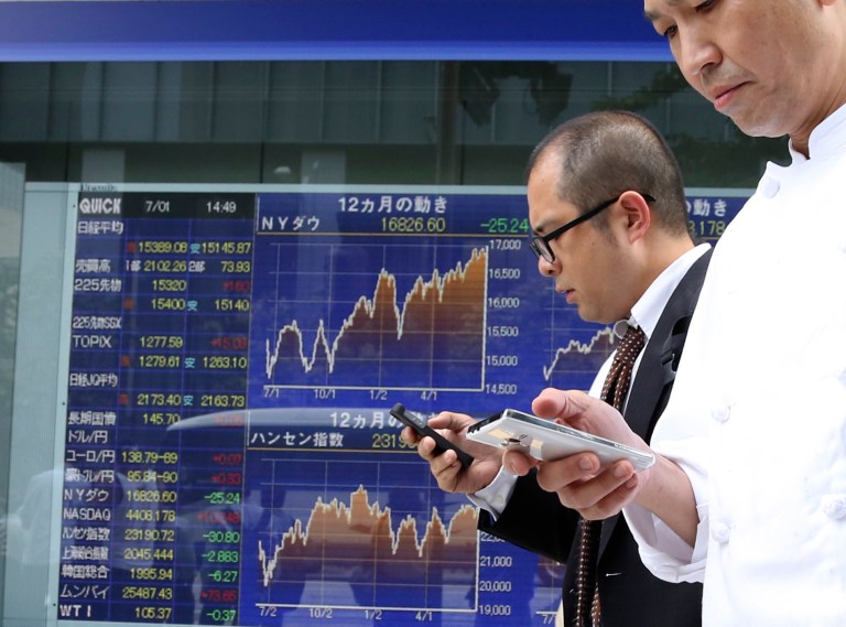Passers-by use cellphones in front of electronic stock board of a securities firm in Tokyo, Tuesday, July 1, 2014. Shares were mostly lower in Asia on Tuesday as investors shrugged off signs that Chinese manufacturing is regaining momentum. (AP Photo/Koji Sasahara)