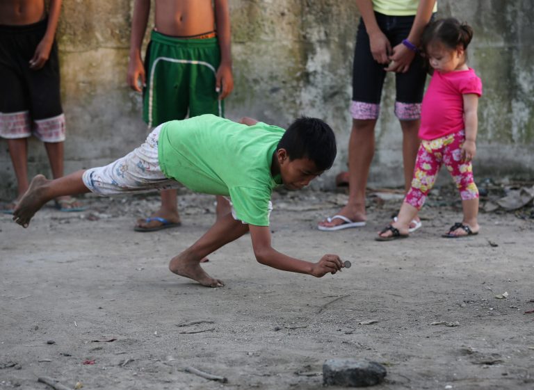 A Filipino boy reaches out to hit his opponents coins during a game which they call Pastra in suburban Malabon, Philippines on Sunday, Aug. 24, 2014. Players try to knock out coins inside a square marked on the ground or hit his opponent's coins to win. Winner gets all the coins in the box. (AP Photo/Aaron Favila)