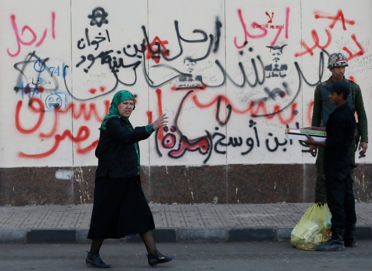   A woman walks past Arabic writings on a wall that read, 