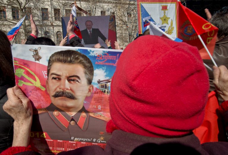 An elderly woman holds a calendar depicting Soviet leader Josef Stalin while watching a large screen showing a broadcast of Russian President Vladimir Putin's speech on Crimea in Sevastopol, Crimea, Tuesday, March 18, 2014 as thousands of pro-Russian people gathered to watch the address. Fiercely defending Russia's move to annex Crimea Putin said Russia had to respond to what he described as a western plot to take Ukraine into its influence.(AP Photo/Vadim Ghirda)