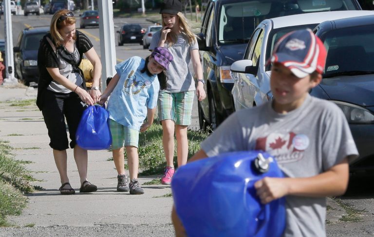 Mary Ellen Kavanaugh, and her children Abby, second from left, Grace and Owen, right, of Windsor, help carry water jugs to St. Peter's Episcopal Church in Detroit, Thursday, July 24, 2014, for a water station being set up to help Detroit residents who need water. A small group of Canadians brought 1,000 liters (264 gallons) of water from Windsor, Ontario, to Detroit to protest thousands of residential service shutoffs by Detroit's water department. (AP Photo)