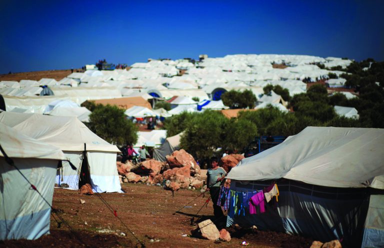 A Syrian boy who fled with his family from the violence in their village, stands next to a tent at a displaced camp, in the Syrian village of Atma, near the Turkish border with Syria, Monday, Nov. 5, 2012. (AP Photo/ Khalil Hamra)