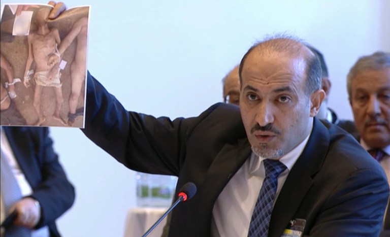 This image taken from UNTV via APTN shows Amhad al-Jarba, the head of Syria's Western-backed Syrian National Coalition, holding up an image of alleged torture victims, during the Syrian peace talks in Montreux, Switzerland, Wednesday Jan. 22, 2014. The peace talks in the Swiss city of Montreux marked the first time the opposition and the Syrian government will sit down face to face since their dispute began in March 2011. (AP Photo/UNTV via APTN)