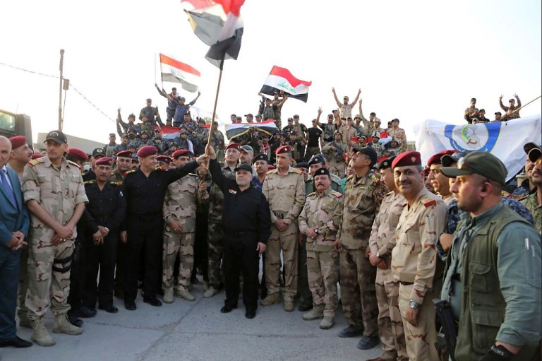 Iraqi Prime Minister Haider al-Abadi raises the national flag on Monday as he addresses forces from a small base on the edge of Mosul's Old City, where heavy clashes have been underway for days. Al-Abadi returned to Mosul Monday and declared victory against the Islamic State group in the northern city following nine months of grueling urban combat. (Iraqi Prime Minister's Media Office via AP)