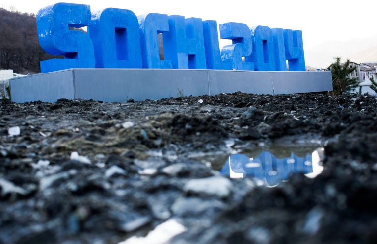 A Sochi 2014 logo of the 2014 Winter Olympics standing on mud and rubble in front of snow-covered mountains is reflected in a puddle, Monday, Feb. 3, 2014, in Krasnaya Polyana, Russia. (AP Photo/Gero Breloer)