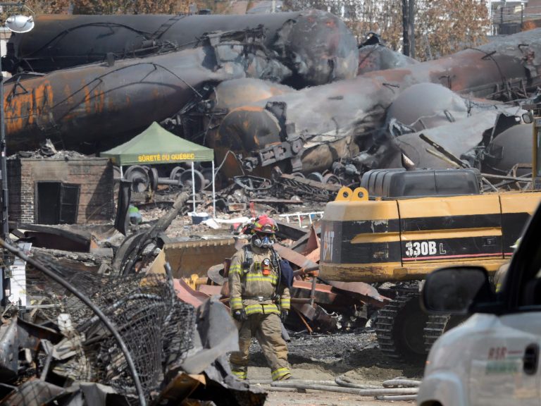 FILE - This July 6, 2013 file photo shows a worker, wearing protective gear moving though the wreckage of the oil train derailment and explosion in  in Lac-Megantic, Quebec. Responding to a series of fiery train derailments, federal regulators said Wednesday they will propose that trains transporting crude oil have at least two-man crews and requirements aimed at preventing parked train cars from coming loose and causing an accident like one in July that killed 47 people. The Federal Railroad Administration had asked a freight rail industry advisory committee to make recommendations on whether two-man crews should be required, but the industry officials were unable to reach a consensus after working on the issue for months. Federal officials said they decided to move ahead with the two-crew member requirement anyway.  (AP Photo/Ryan Remiorz, File, Pool)