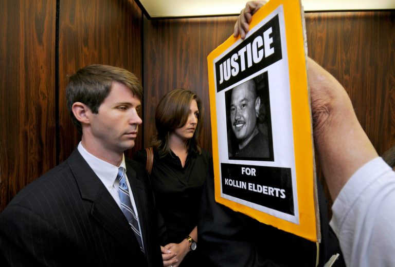 FILE- In this Nov. 17, 2011 file photo, an unidentified protester shoves a sign in the face of State Department Special Agent Christopher Deedy, left, and his wife on an elevator in Honolulu. Deedy, of Arlington, Va., is back in Honolulu to stand trial a second time for killing Kollin Elderts during an altercation in a McDonald's restaurant. He contends the shooting was self-defense. Free on $250,000, bail, he returned home after the first trial. (AP Photo/Honolulu Star Advertiser, Dennis Oda, File)