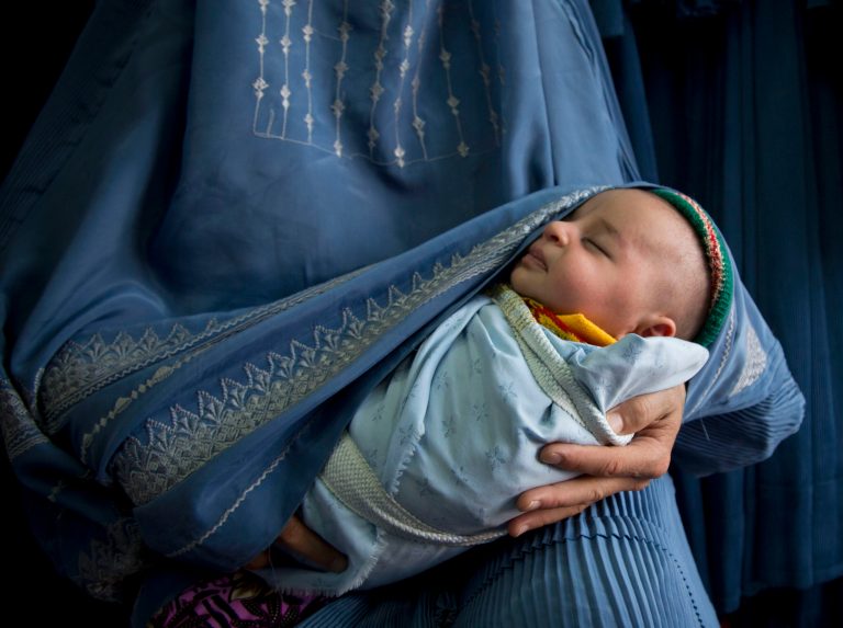 In this Thursday, April 11, 2013 photo, an Afghan woman holds her newly born baby wrapped in her burqa as she waits to get in line to try on a new burqa in a shop in the old town of Kabul, Afghanistan. Despite advances in women's rights, Afghanistan remains a deeply conservative country and most women continue to wear the Burqa. But tradesmen say times are changing in Kabul at least, with demand for burqas declining as young women going to school and taking office jobs refuse to wear the cumbersome garments. (AP Photo/Anja Niedringhaus)