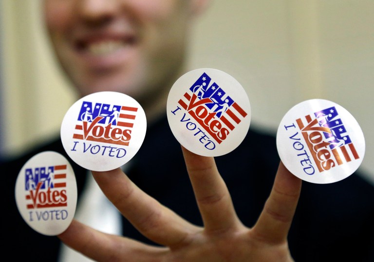 Seth Schaecher, a deputy election official, displays stickers that he gives to voters, Tuesday, Nov. 8, 2016, at a polling place in Exeter, N.H. (AP Photo/Elise Amendola)