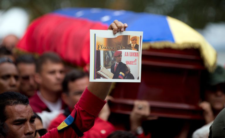A person holds up a photograph of former Venezuelan Intelligence Chief Eliezer Otaiza as his flag-draped coffin is carried outside the National Assembly during his funeral procession in Caracas, Venezuela, Wednesday, April 30, 2014. Otaiza's body was dumped on the edge of Caracas Saturday after his vehicle was intercepted by a group of armed men. No motive has been established for the crime. As a young army officer, he backed Hugo Chavez's failed 1992 coup attempt and was responsible for his personal security when he was elected president in 1998. (AP Photo/Fernando Llano)
