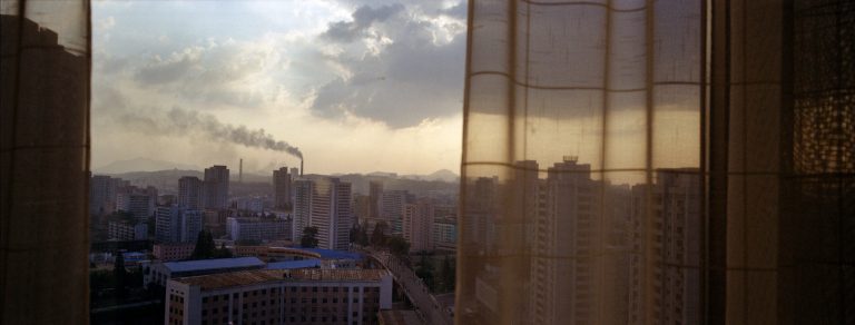   In this Aug. 7, 2012 photo, the sun sets over Pyongyang, North Korea, behind the curtained window of a downtown hotel room. (AP Photo/David Guttenfelder)  