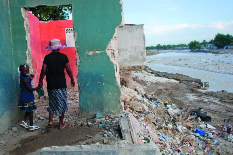 Jesumene St-Fleur, 48, walks with her five-year-old daughter Marie Lourdine at their home that was damaged by heavy rain brought by Hurricane Sandy in Port-au-Prince, Haiti, Monday, Nov. 12, 2012. The rain has tapered off and floodwaters no longer claw at houses, but the situation across much of Haiti remain grim, following an autumn of punishing rains that have killed scores of people and that threaten to cause even more hunger across the nation. (AP Photo/Dieu Nalio Chery)
