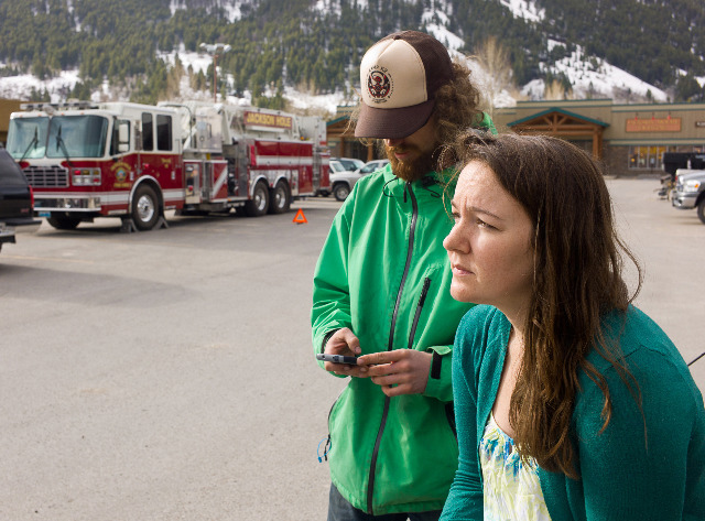 Kristin Livingstone, right, watches her evacuated hillside neighborhood after spending a night away from her home because of danger from a potential landslide in Jackson, Wyo., Thursday, April 10, 2014. Brendon Newton, left, gets in touch with others at an assembly point in a parking lot across the street from the threatened slope. Dozens of Jackson residents who were evacuated after land began shifting on the hillside. (AP Photo/Jackson Hole News & Guide, Angus M. Thuermer Jr.)