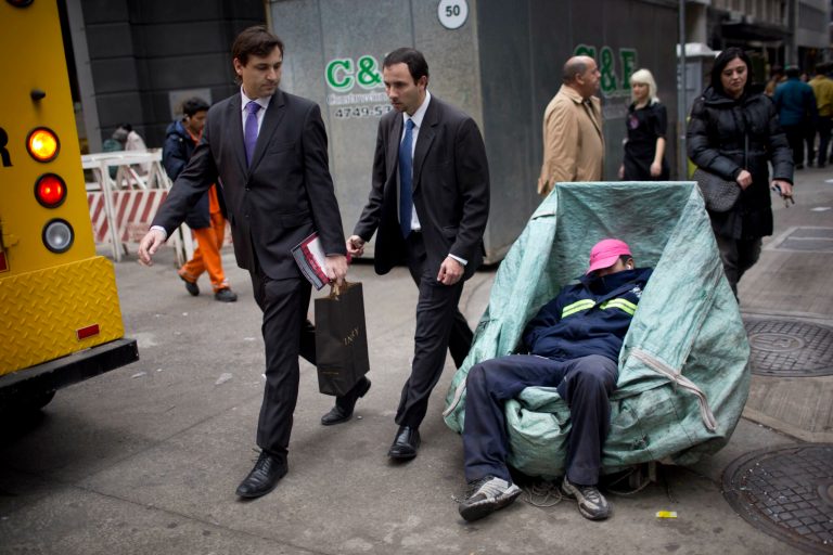An office worker looks at a man sleeping inside the basket he uses to collect cardboard for recycling at the financial district in Buenos Aires, Argentina, Thursday, July 31, 2014. The collapse of talks with U.S. creditors sent Argentina into its second debt default in 13 years and raised questions about what comes next for financial markets and the South American nation's staggering economy. (AP Photo/Rodrigo Abd)