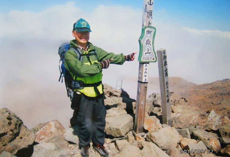 FILE - In this Saturday, Sept. 27, 2014 file photo found in a camera possessed by 59-year-old hiker Izumi Noguchi, a construction worker, who fell victim to the eruption of Mount Ontake, and was offered to Kyodo News by his wife, Hiromi, Friday, Oct. 3, Noguchi poses on the summit of Mount Ontake shortly before the eruption of the volcanic mountain in central Japan. Noguchi was climbing alone, as his usual hiking companion, his wife Hiromi, had to work, she told Japanese broadcaster NHK and other TV stations. His compact camera was banged up, but the memory chip inside was undamaged. She printed all 100 shots. The last one is of an enormous plume billowing from the crater behind a mountaintop lodge. (AP Photo/Kyodo News, File) JAPAN OUT, MANDATORY CREDIT