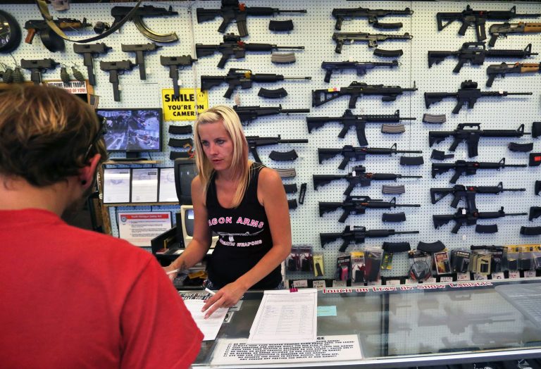 In this July 20, 2014 photo, with guns displayed for sale behind her, a gun store employee helps a customer at Dragonman's, east of Colorado Springs, Colo. (AP Photo/Brennan Linsley)