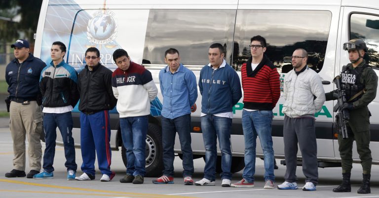 Police flank seven men accused of murdering a Drug Enforcement Administration agent, during a media presentation at the counter-narcotics base in Bogota, Colombia, Tuesday, July 1, 2014, prior to their extradition to the United States. The men are accused of killing Special Agent James 