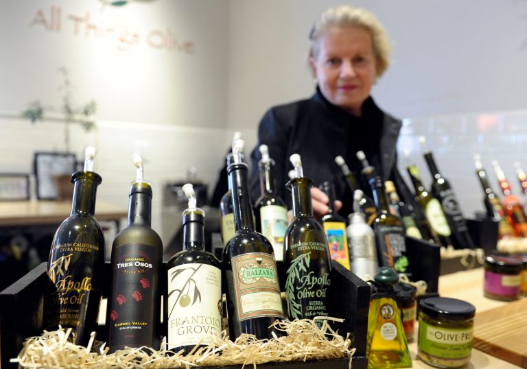 This photo taken Feb. 12, 2014 shows California Olive Oil Council Executive Director Patricia Darragh posing with a collection of California olive oil at the All Things Olive shop in Washington. It's a pressing matter for the tiny U.S olive oil industry. Shoppers are more often pouring European oil _ it's cheaper and viewed as more authentic than the American competition. And that's pitting U.S. producers against importers of the European oil. Some liken the battle to the California wine industry's struggles to gain acceptance decades ago. The tiny California olive industry says European olive oil filling U.S. shelves often is mislabeled and lower grade. They're pushing the federal government to give more scrutiny to imported varieties. One congressman-farmer even goes as far as suggesting labels on imported oil say 