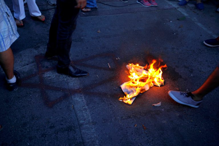 Protestors burn a hand-painted Israeli flag next to a graffiti of the Star of David symbol, seen on the ground, during an anti Israel demonstration outside of the Israeli embassy in Nicosia, Cyprus, Monday, July 21, 2014. Several hundred pro-Palestinian protesters demanded a halt to military action in Gaza during a peaceful protest near the Israeli embassy in the Cypriot capital. (AP Photo/Petros Karadjias)