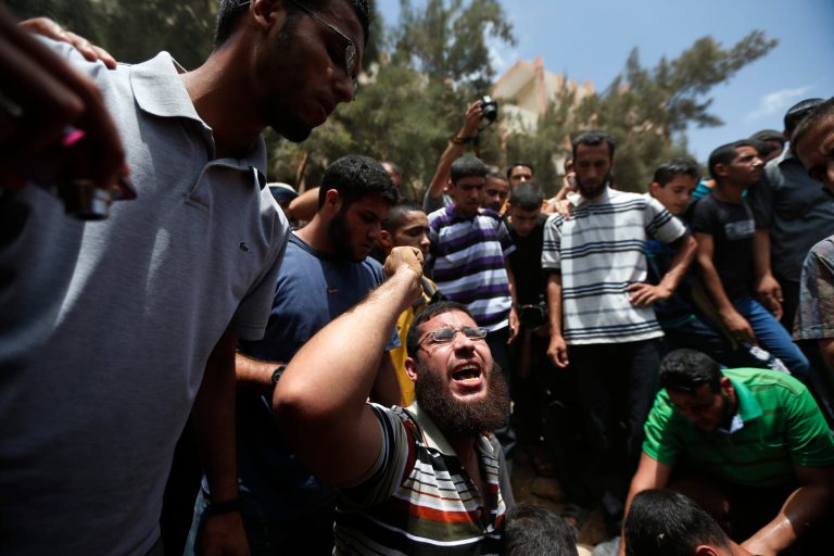 A Palestinian mourner chants slogans on the grave of a member of the al-Batsh family who were killed in Saturday's Israeli airstrike, during a funeral procession in Gaza City on Sunday, July 13, 2014. The strike hit the home of Gaza police chief Taysir al-Batsh and damaged a nearby mosque as evening prayers ended Saturday, killing at least 18 people, wounding 50 and leaving some people believed to be trapped under the rubble, said Palestinian Health Ministry official Ashraf al-Kidra. (AP Photo/Lefteris Pitarakis)